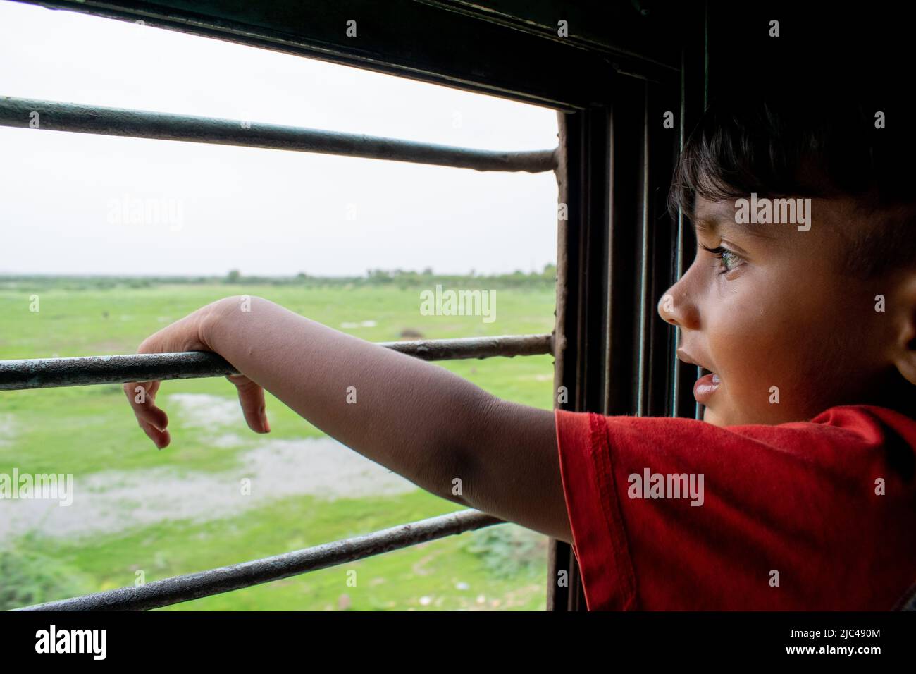 Ein indischer Junge im Zug, der durch das Fenster nach draußen schaute und die Fahrt genoss Stockfoto