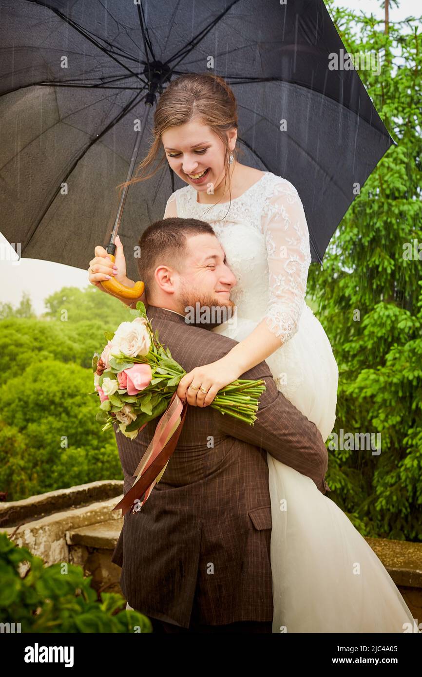 Das Brautpaar spaziert an einem grünen Sommertag mit einem Regenschirm im grünen Park Stockfoto