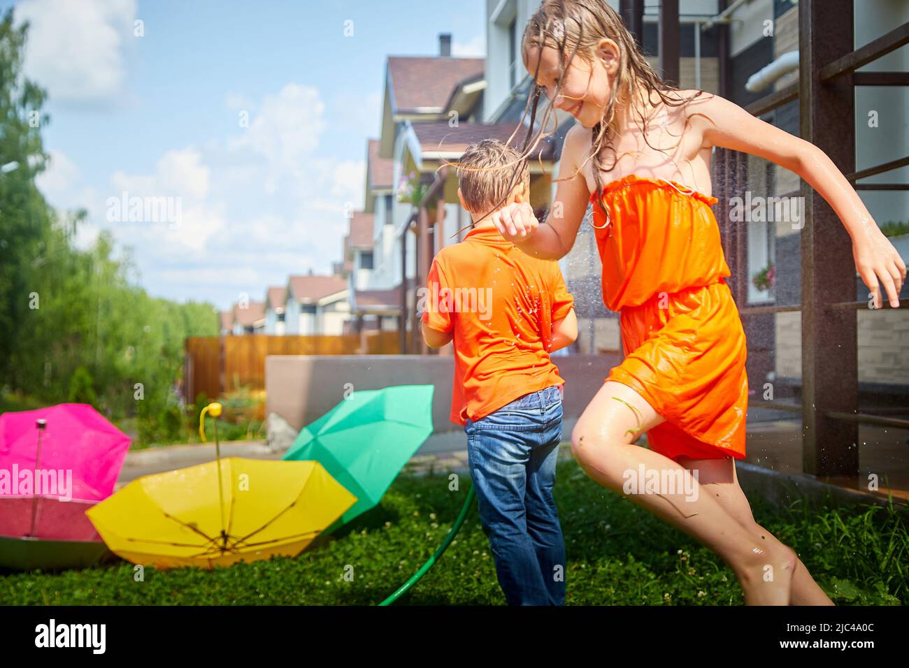 Kinder spielen mit Gartenregner. Bruder und Schwester laufen und springen. Sommer im Freien Wasser Spaß im Hinterhof. Junge und Mädchen spielen mit Schlauch Stockfoto