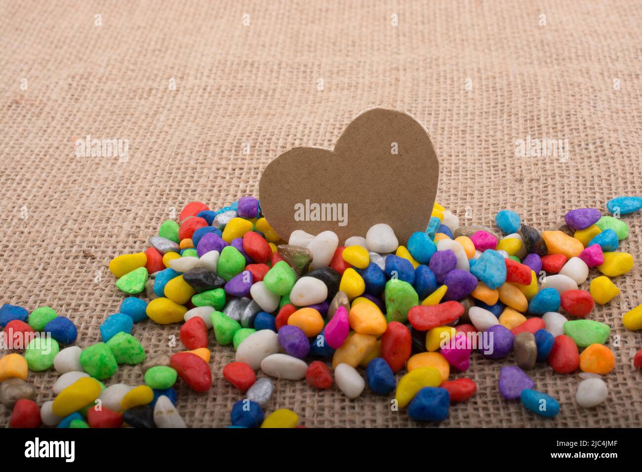 Herz aus Papier inmitten der bunten Steinchen auf Leinwand Boden Stockfoto