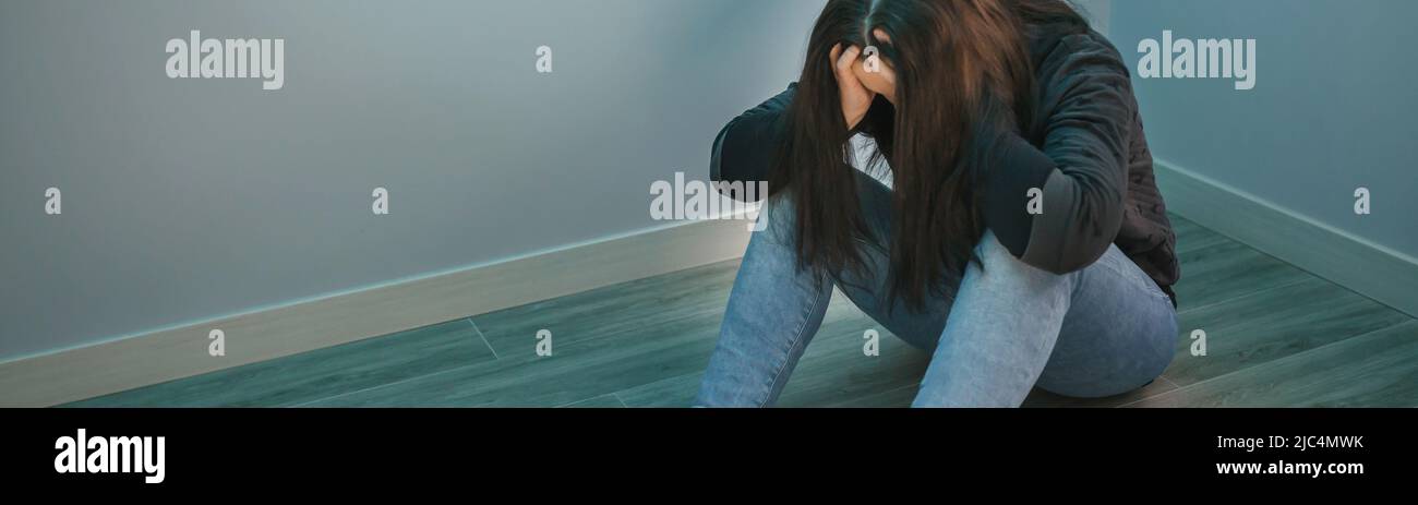 Frau mit psychischen Problemen mit Händen im Kopf auf dem Boden sitzend Stockfoto