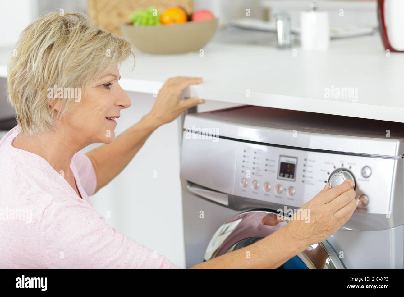 Reife Frau, die ihre Waschmaschine kontrolliert Stockfoto