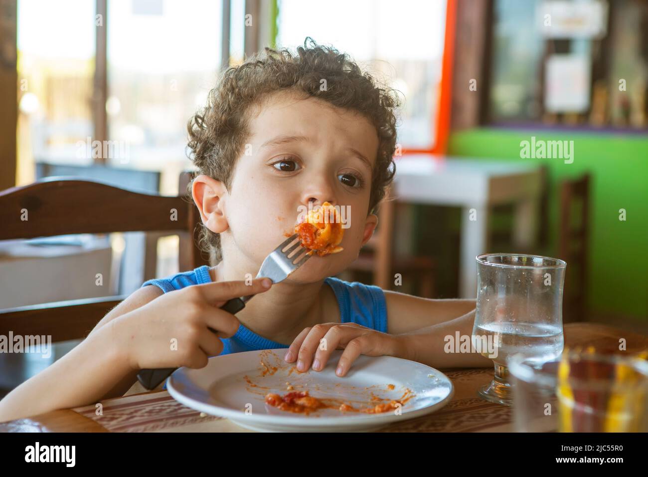 Komischer, lockiger Junge, der Tortellini im Restaurant isst Stockfoto