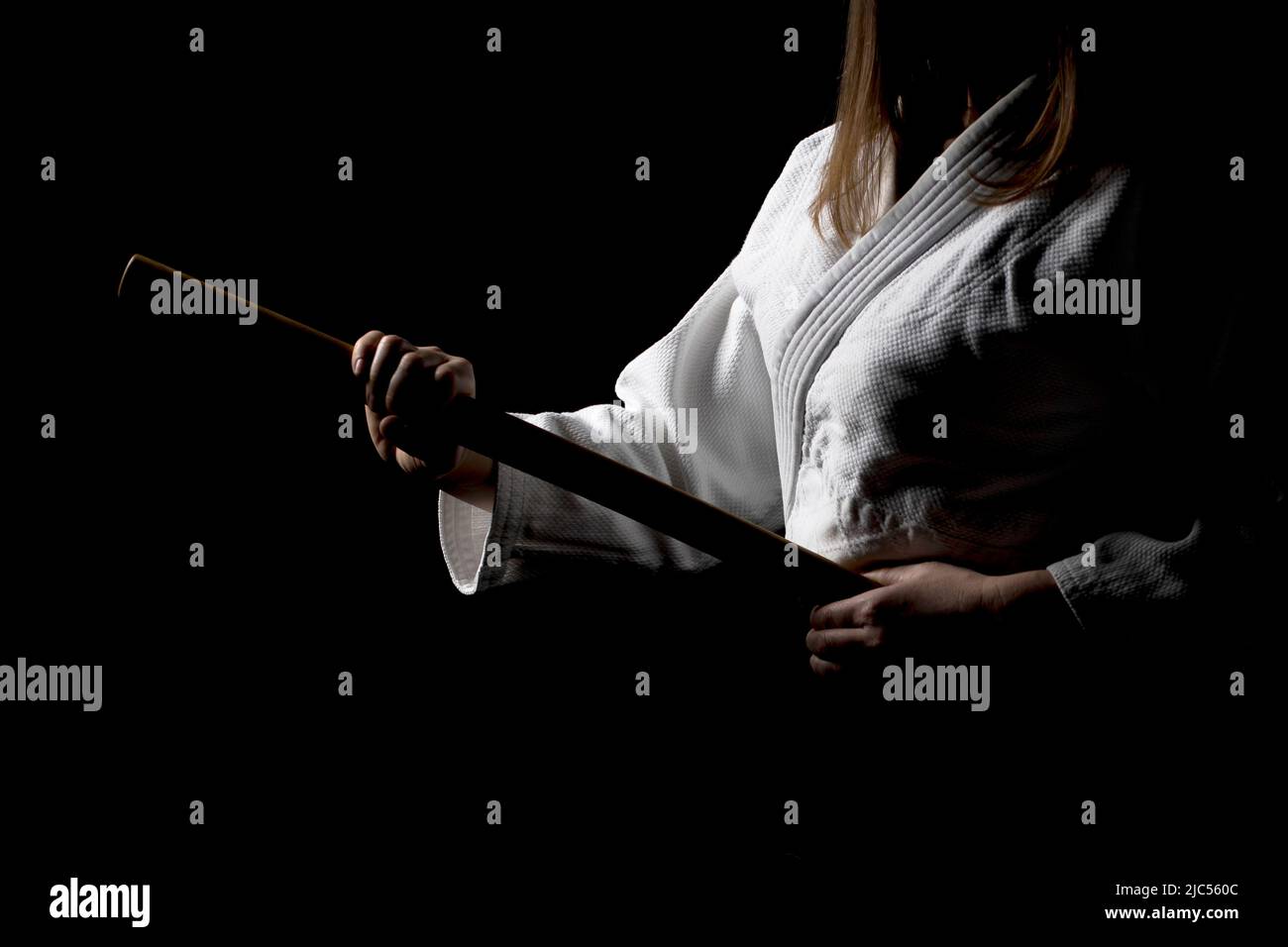 Ein Mädchen in schwarzem Hakama, das in kämpfender Pose mit Holzschwert auf dunklem Hintergrund bokken steht. Geringe Schärfentiefe. SDF. Stockfoto