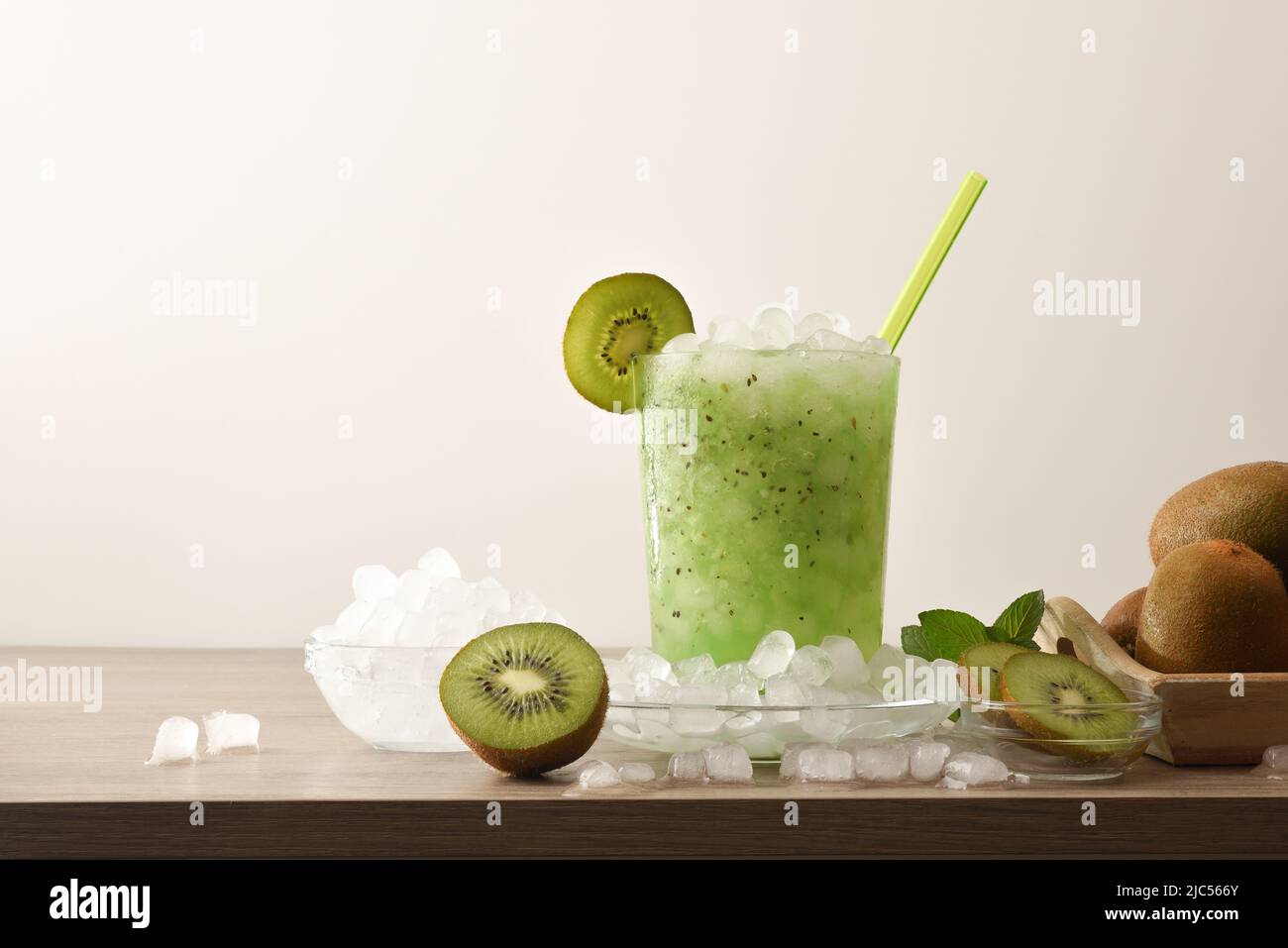 Kiwi Slush trinken im Glas mit Früchten und zerkleinerten Eis um ihn herum auf Holztisch mit isoliertem Hintergrund. Vorderansicht. Horizontale Zusammensetzung. Stockfoto