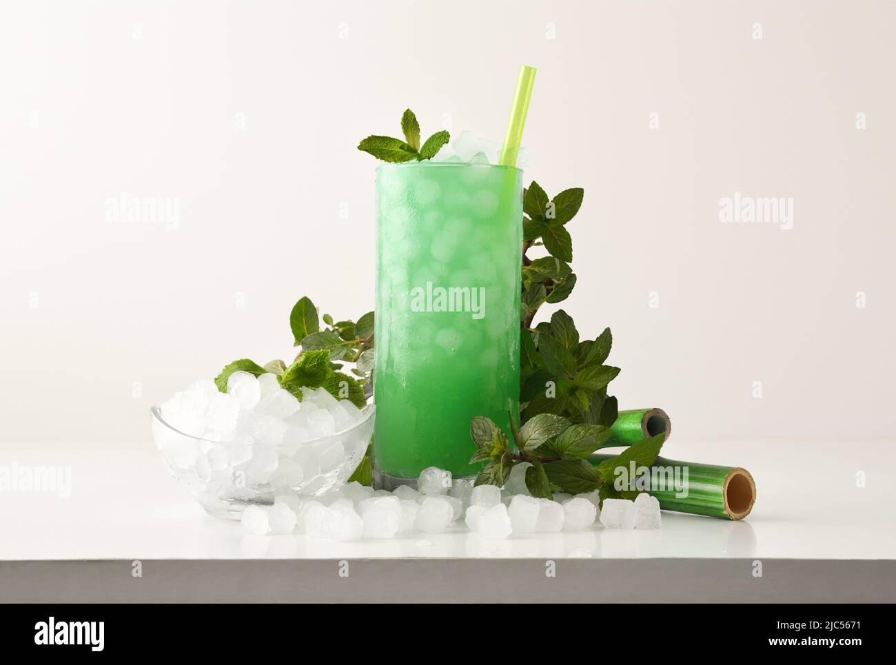 Minze Slush trinken in hohem Glas mit Blättern und zerkleinerten Eis um ihn herum auf weißem Tisch mit isoliertem Hintergrund. Vorderansicht. Horizontale Zusammensetzung. Stockfoto
