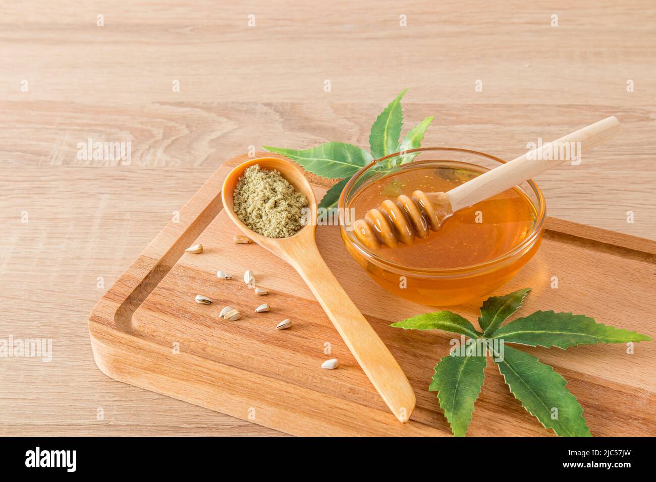 Transparenter Bernsteinhonig mit den Produkten der Morajuana-Verarbeitung in einem Glasgefäß auf einem Holzbrett und einem Tisch mit den Blättern der Pflanze. CBD Stockfoto