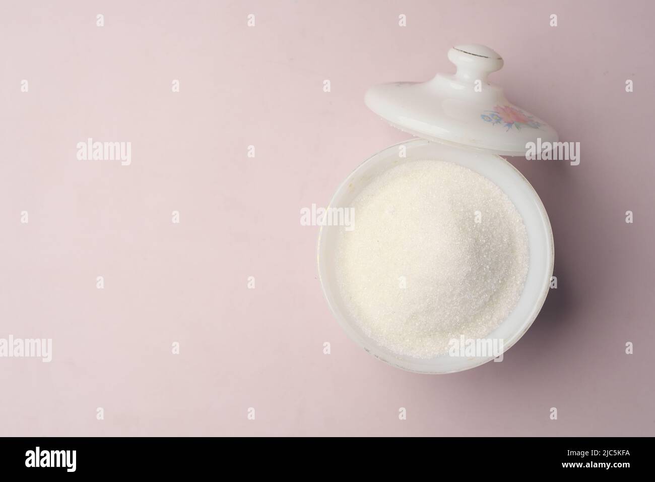 Weißer Zucker und Löffel in einem Behälter auf schwarzem Hintergrund, Stockfoto
