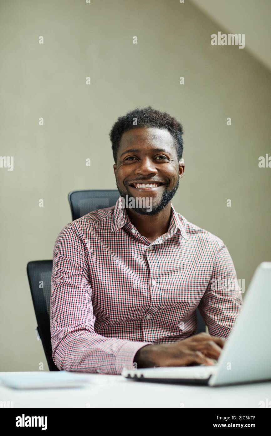 Porträt eines jungen, bärtigen afroamerikanischen IT-Ingenieurs, der in einem modernen Büro vor einem Laptop sitzt Stockfoto