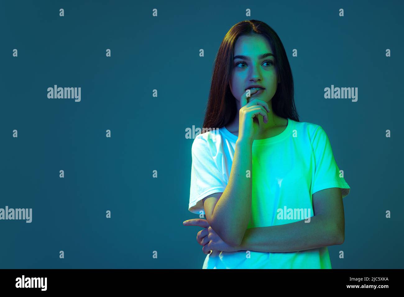 Junge schöne Mädchen mit langen Haaren Denken isoliert auf blauem Hintergrund in Neonlicht. Konzept von Schönheit, Kunst, Mode, Emotionen Stockfoto