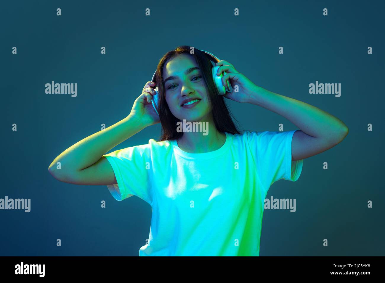 Portrait von attraktiven jungen Mädchen mit langen lockeren Haaren hören Musik isoliert auf blauem Hintergrund in Neonlicht. Konzept von Schönheit, Kunst, Mode Stockfoto