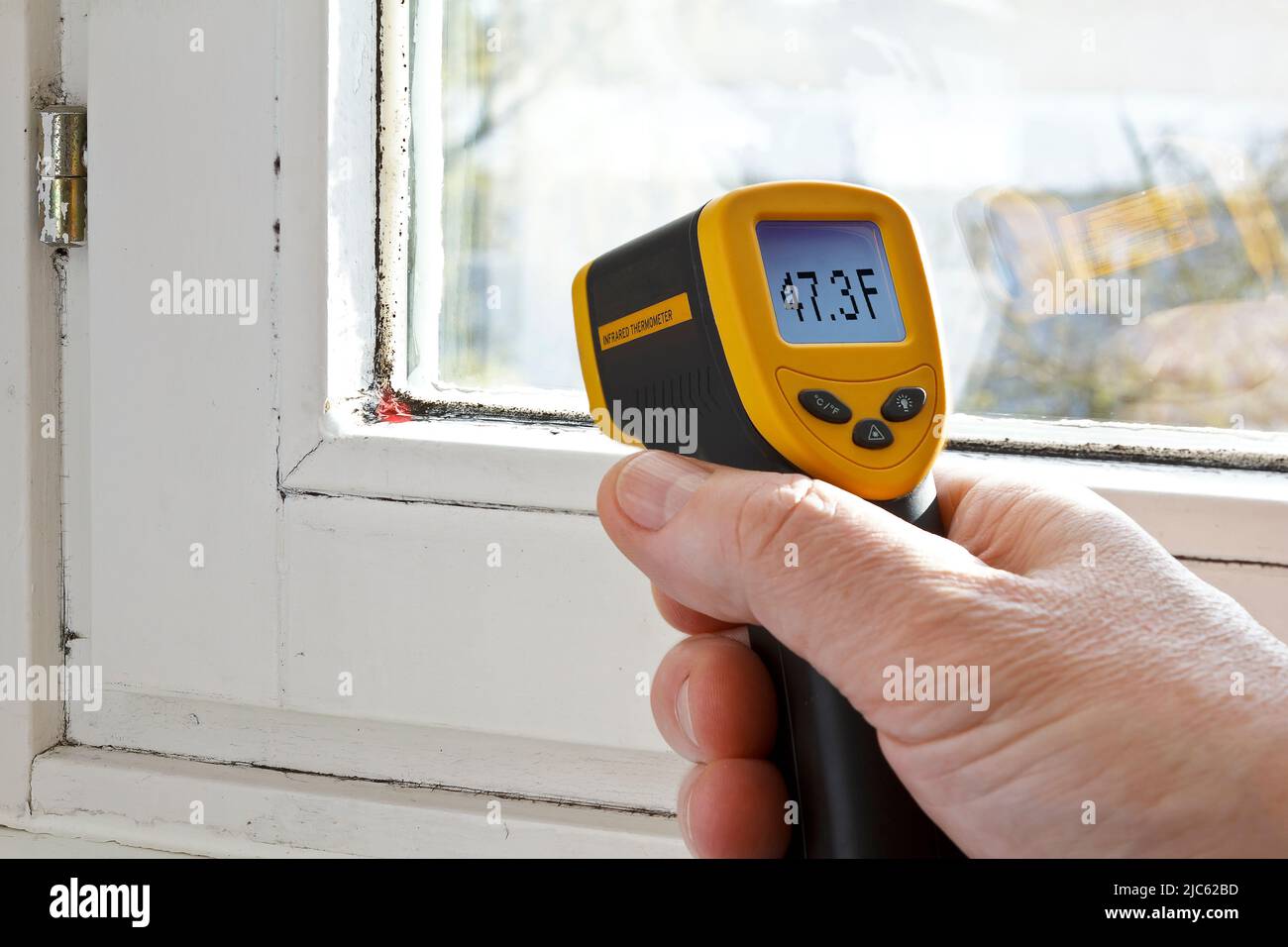 Männliche Hand mit einem Infrarot- oder Laserthermometer zur Messung der Temperatur einer Fensterdichtung, wo Schimmel wächst. Stockfoto