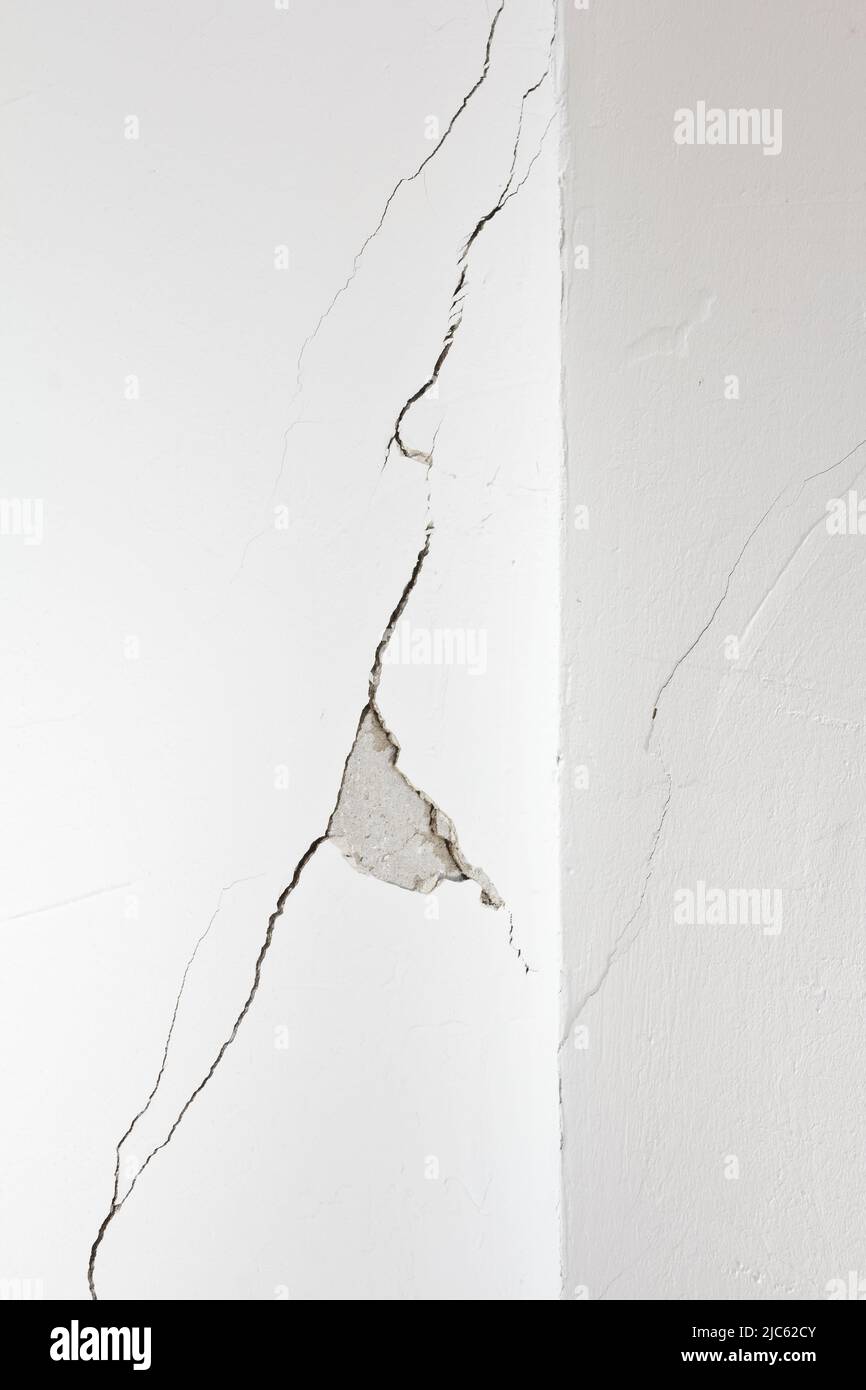 Beschädigte weiße Wand mit einem langen Riss oder Riss und einem Stück Gips fehlt. Konzept der Sanierung, Renovierung oder Umstrukturierung von Immobilien. Stockfoto
