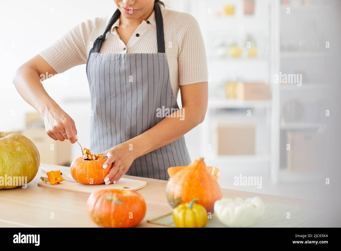 Nahaufnahme einer zufriedenen Frau in der Schürze, die an der Theke in der Küche steht und Kürbiskerne ausschaufelt Stockfoto