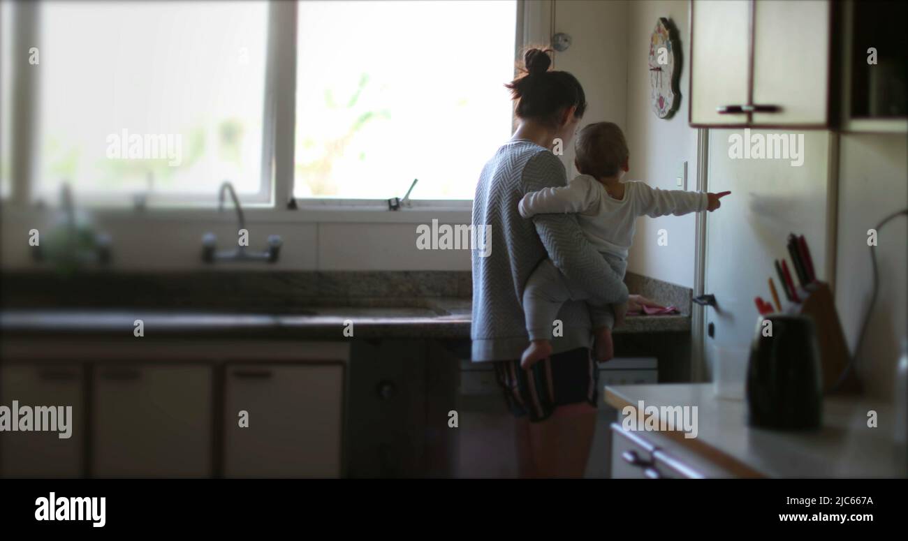 Lässige Mutter hält Baby in der Küche Multitasking. Elternteil zu Hause mit Säuglingsreinigung Stockfoto