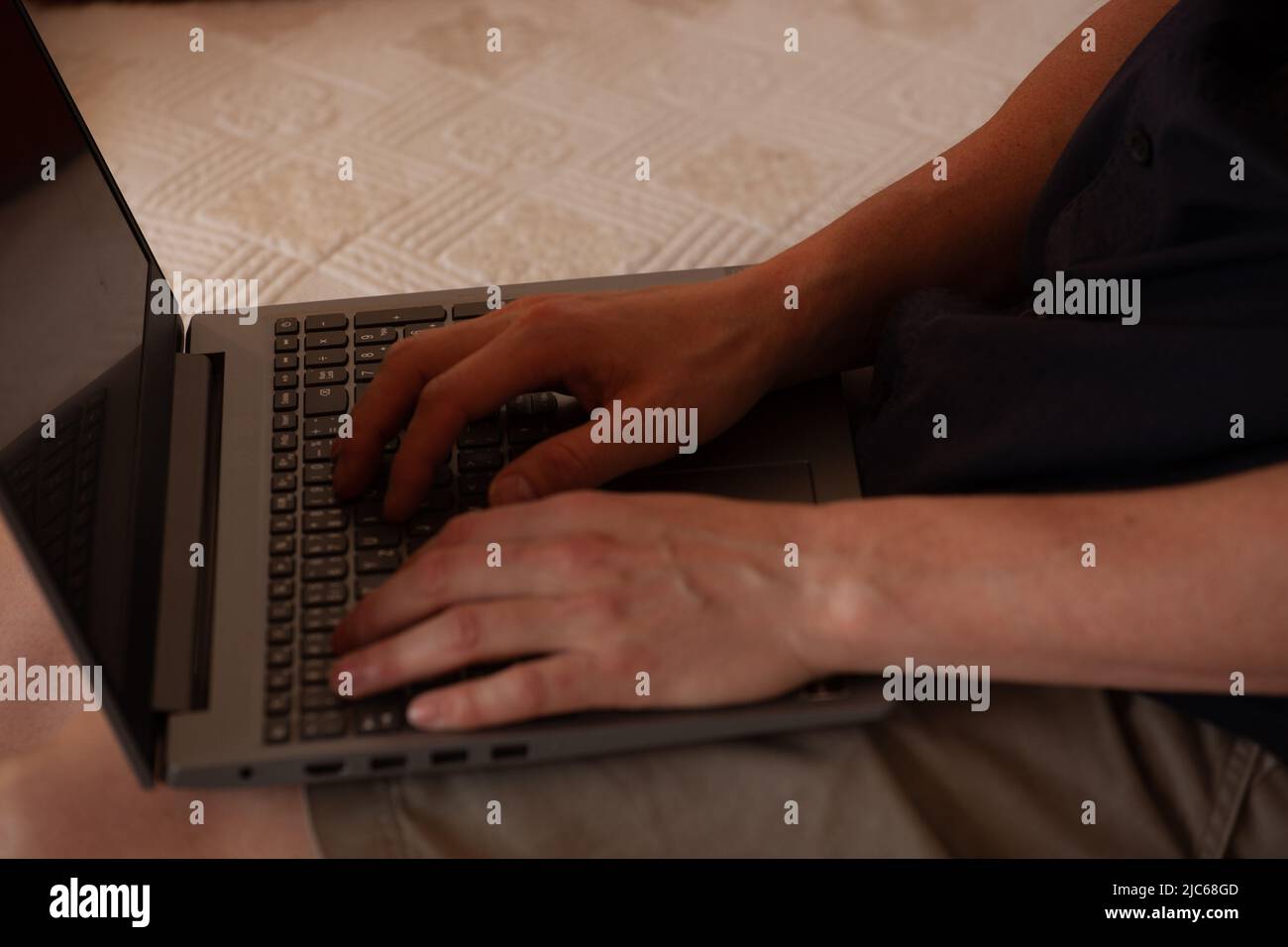 Die Hände eines Mannes auf einer Computertastatur. Ein weißhäutiger Mann tiptet auf die Tasten einer Laptop-Tastatur. Er sitzt auf einem weißen Sofa. Wir können sein Gesicht nicht sehen Stockfoto