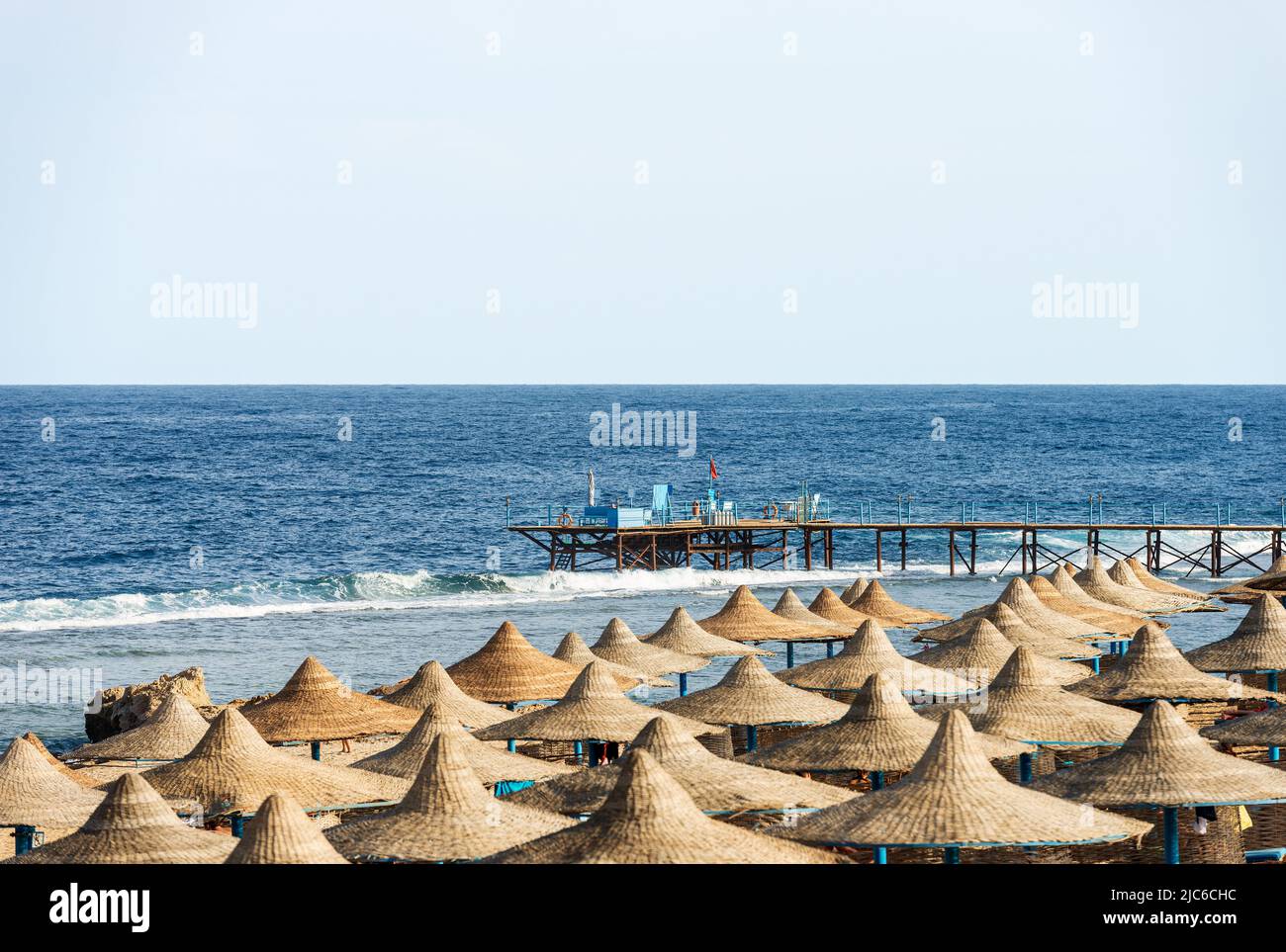 Rotes Meer und Strand mit Strohschirmen in der Nähe von Marsa Alam, Ägypten, Afrika. Meereslandschaft und Wellen brechen auf dem Korallenriff. Stockfoto