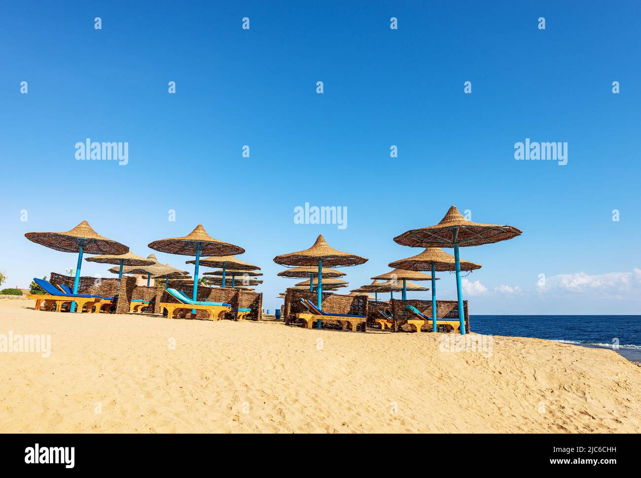 Sandstrand am Roten Meer mit Strohschirmen und Liegestühlen in der Nähe von Marsa Alam, Ägypten, Afrika. Meereslandschaft und Wellen brechen auf dem Korallenriff. Stockfoto