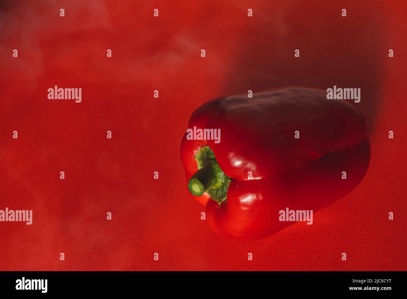 SÜSSER, FRISCHER ROTER PFEFFER AUF ROTEM HINTERGRUND MIT LEICHTEM RAUCH. Stockfoto