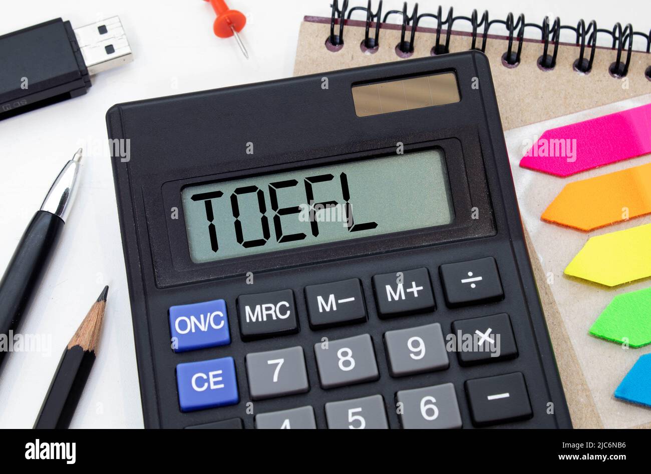 TOEFL - Test of English as a Foreign Language. Text auf weißem Papier auf hellweißem Hintergrund. Im Hintergrund ist eine Lupe, ein Diagramm, eine Kalk Stockfoto