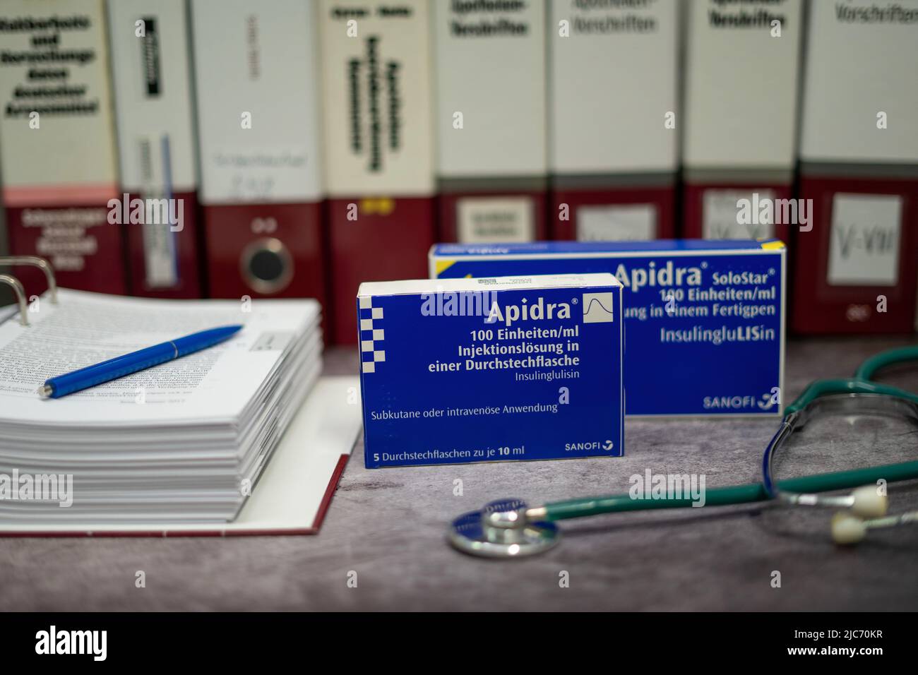 Apidra-Medikament, das schnell wirkendes Insulin zur Behandlung von Diabetes mellitus enthält, auf einem Tisch und im Hintergrund verschiedene medizinische Bücher. Stockfoto