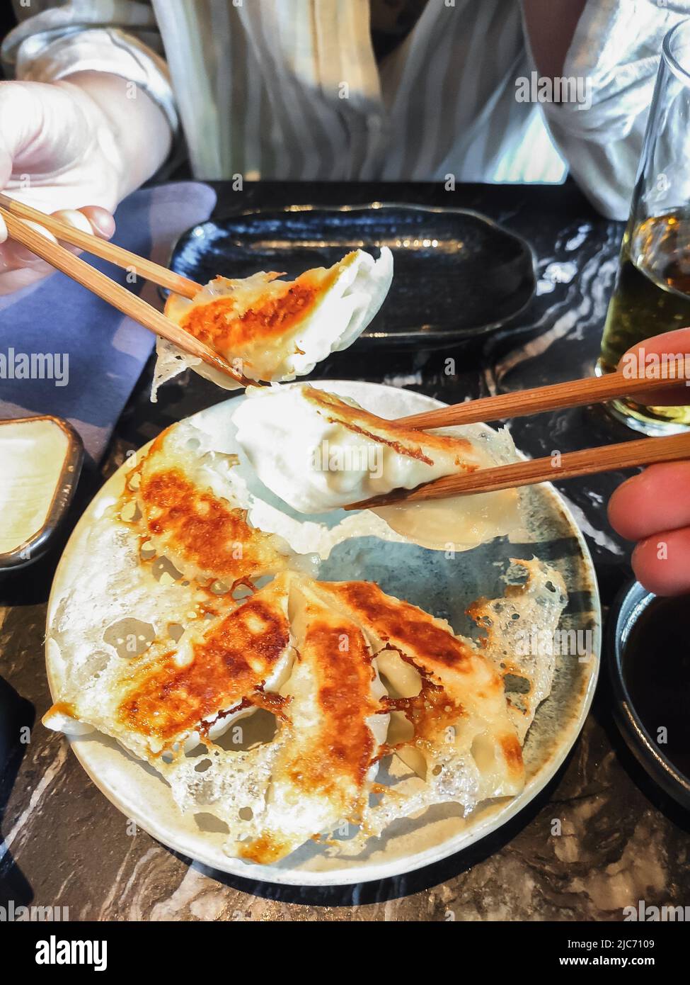 Nahaufnahme von zwei Händen, die Essstäbchen mit köstlichen Gyoza, japanischen Knödeln im Restaurant halten Stockfoto