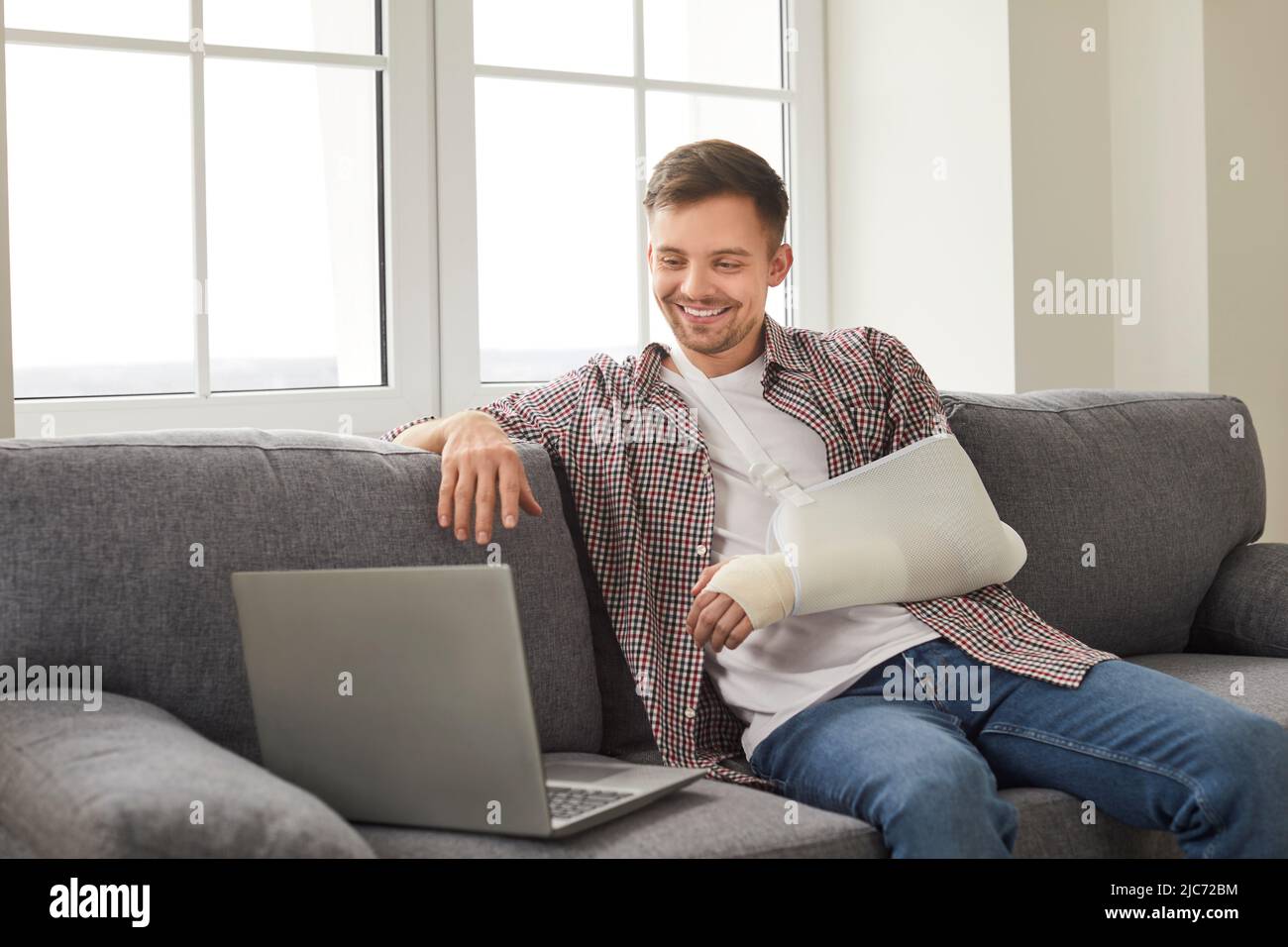 Mann mit gebrochenem Arm, der Filme auf einem Laptop ansieht oder zu Hause über einen Videolink mit Freunden spricht. Stockfoto