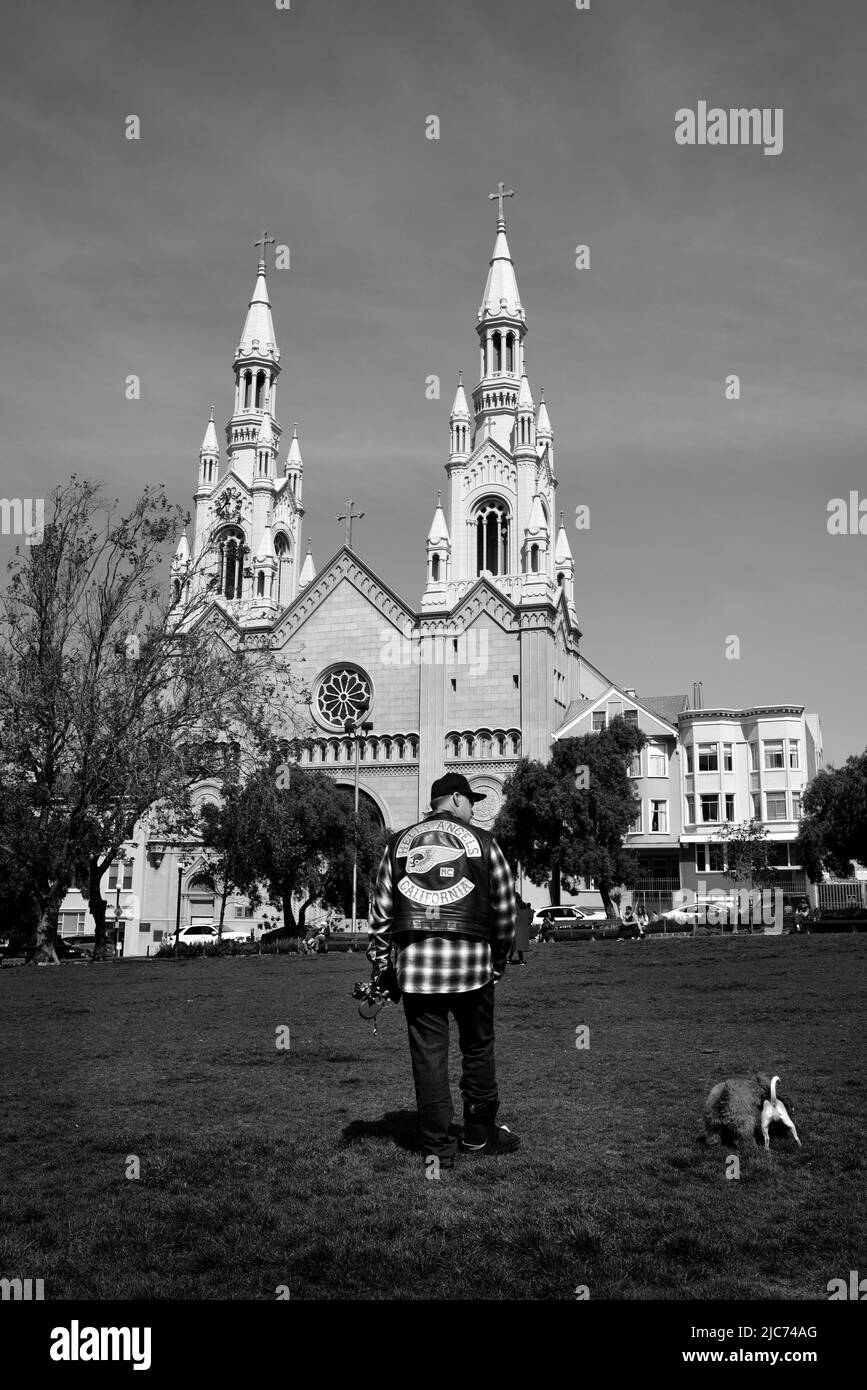 Ein Mann mit einer Motorrad-Clubjacke von Hell's Angels geht mit seinem Hund vor die Saints Peter and Paul Church in San Francisco, Kalifornien. Stockfoto
