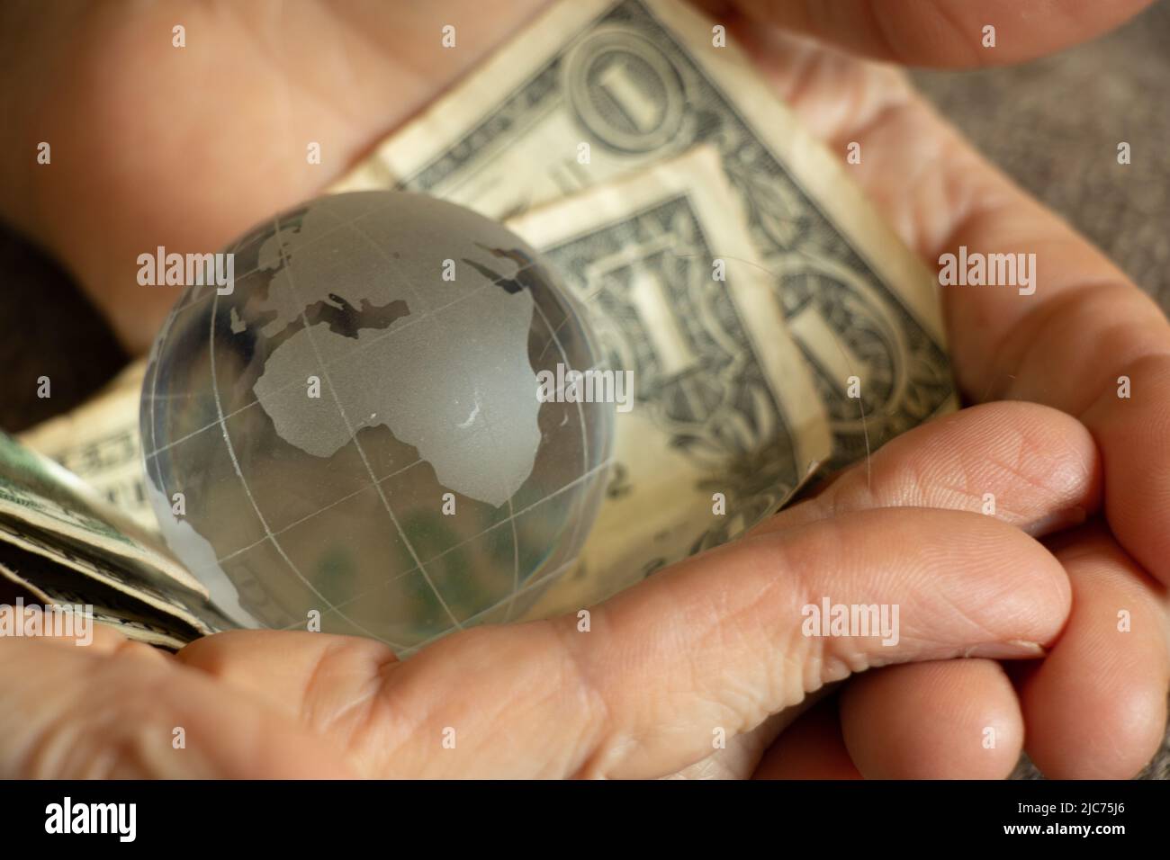 amerikanische Dollar und eine Glaskugel des Planeten liegen in den Händen einer alten Frau, Finanzwelt und Menschen Stockfoto