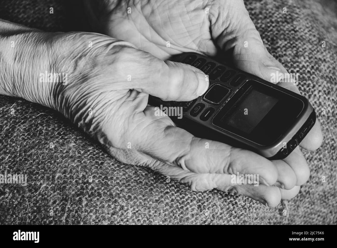 Die Hände der alten Frau halten das Telefon zu Hause, die Rentnerin mit dem Telefon Stockfoto