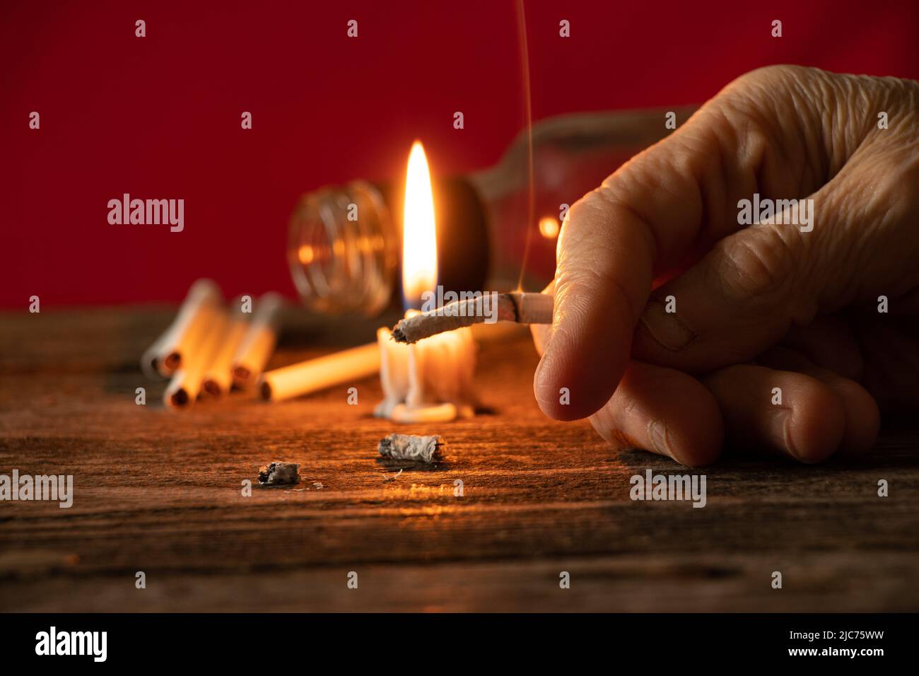 Alte Frau hält eine Zigarette bei Kerzenlicht im Dunkeln zu Hause am Tisch, Rauchen zu Hause im Dunkeln, Nikotin und schlechte Angewohnheit, Zigaretten und Dose Stockfoto