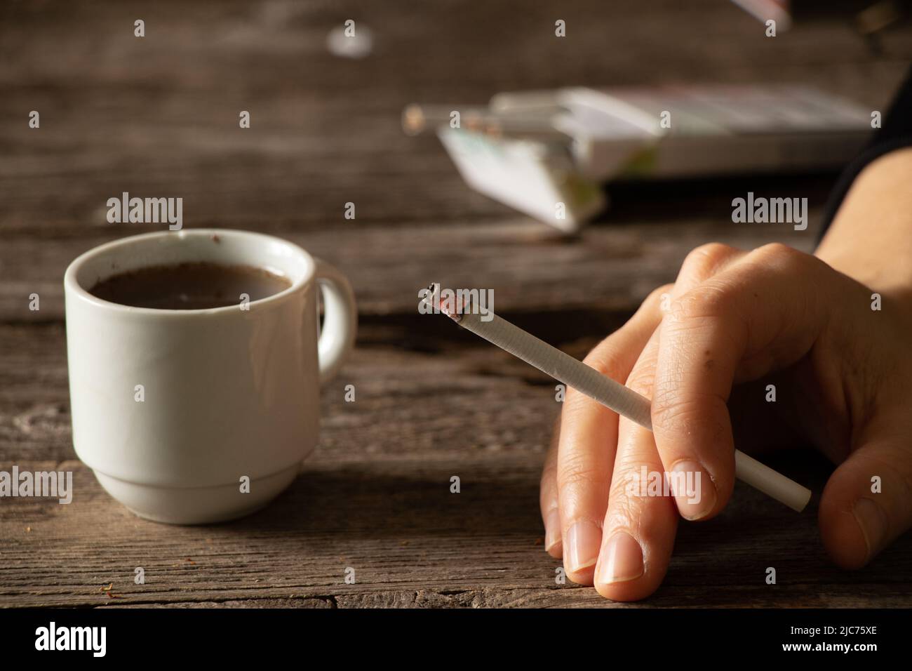 Eine Zigarette in den Händen eines Mädchens auf dem Tisch neben einer Tasse Kaffee, Zigaretten und Kaffee, schlechte Gewohnheiten, Rauchen Stockfoto