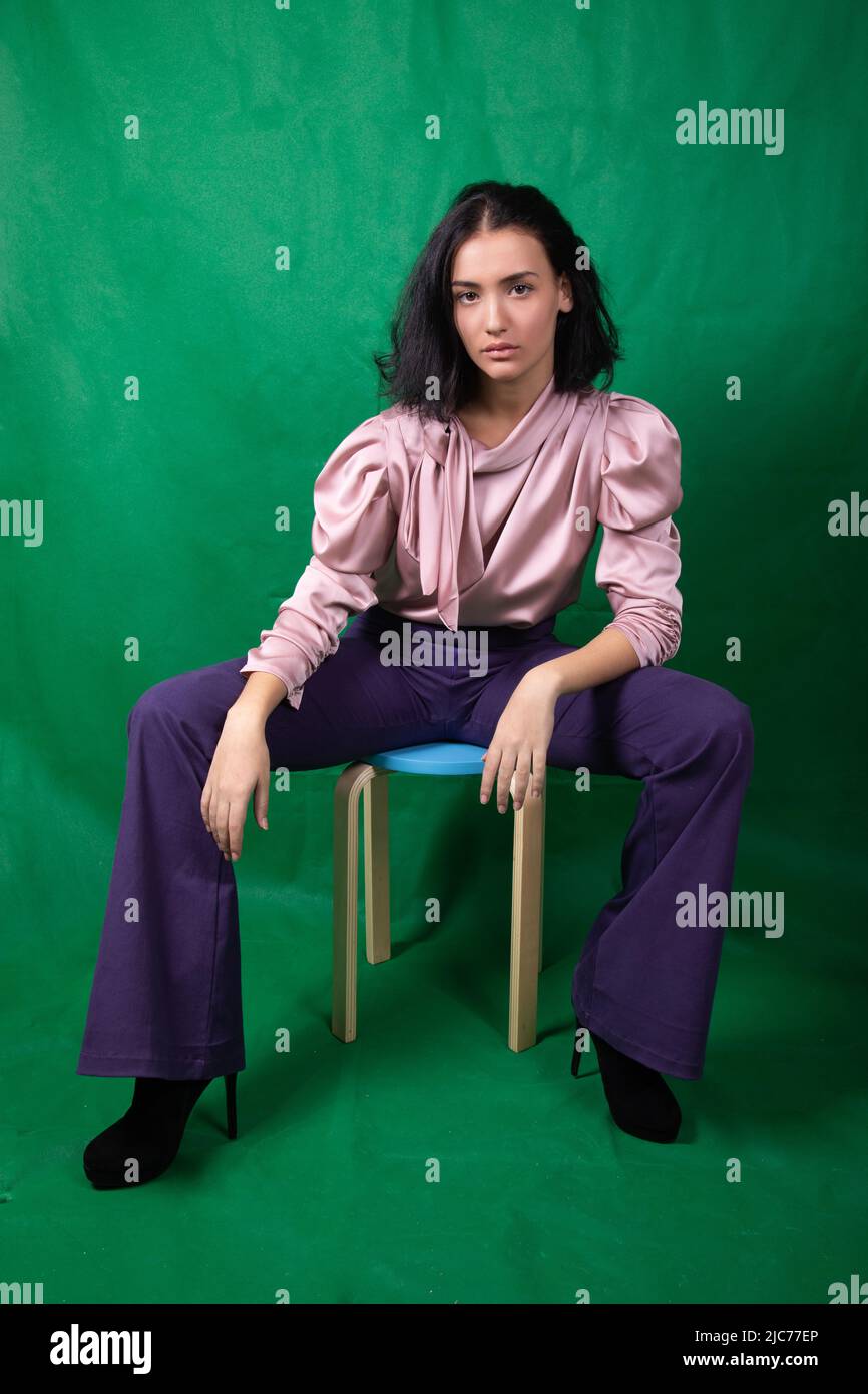 Junge hübsche Model sitzt auf einem blauen Hocker und ruht ihre Ellbogen auf den Knien im Studio Stockfoto