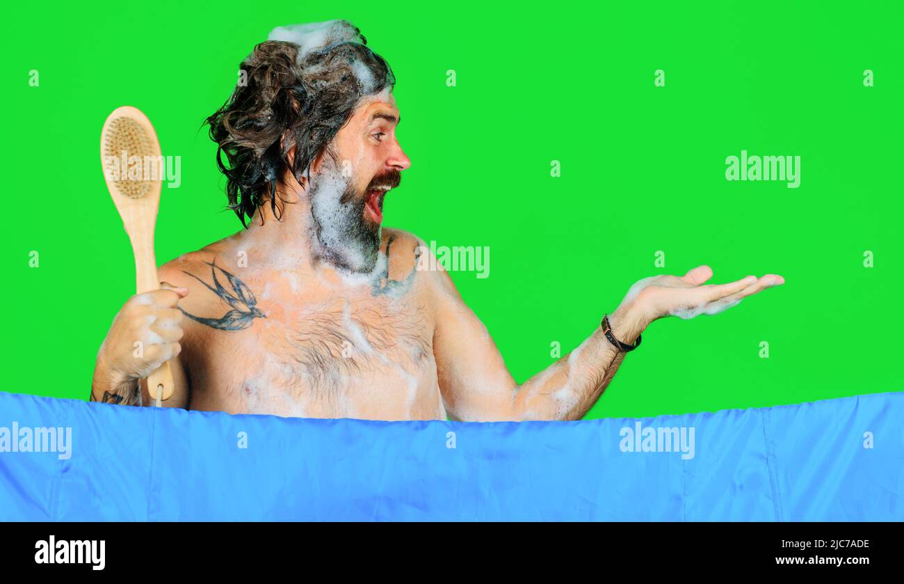 Ein glücklicher bärtiger Mann, der sich duscht, hält etwas auf der Handfläche. Badezeit. Werbung. Speicherplatz kopieren. Stockfoto