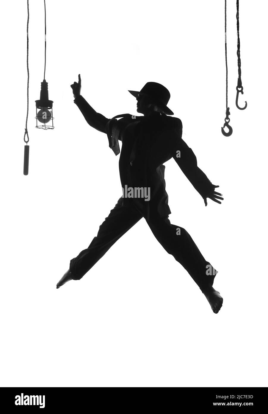 Eine Tänzerin wird auf der Bühne getanzt. In Herrenbekleidung gekleidet und mit einem Männerhut bekleidet, sieht man sie als Silhouette in der Luft springen. Stockfoto