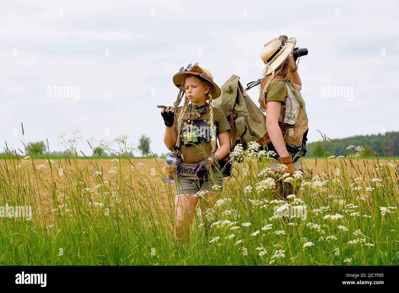 Zwei junge Mädchen werden als Entdecker gesehen. Sie beobachten die Landschaft im Freien. Sie sind mit Safarihüten, Ferngläsern und Khaki-Safari-Outfits gekleidet. Stockfoto