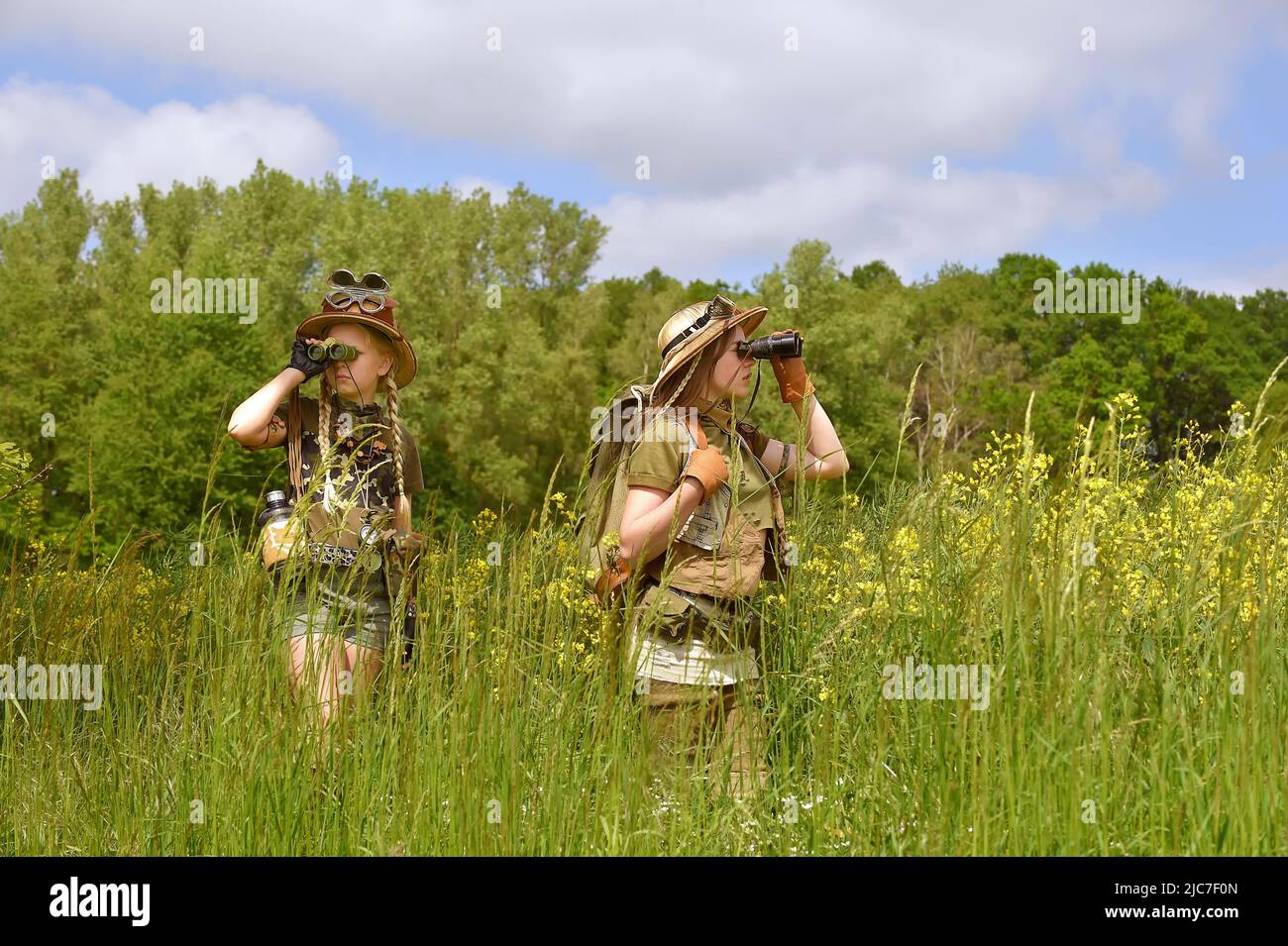 Zwei junge Mädchen werden als Entdecker gesehen. Sie beobachten die Landschaft im Freien. Sie sind mit Safarihüten, Ferngläsern und Khaki-Safari-Outfits gekleidet. Stockfoto