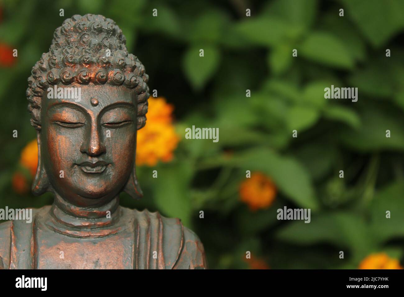 Buddha Statue im Garten mit verschwommenen Blumen im Hintergrund Stockfoto