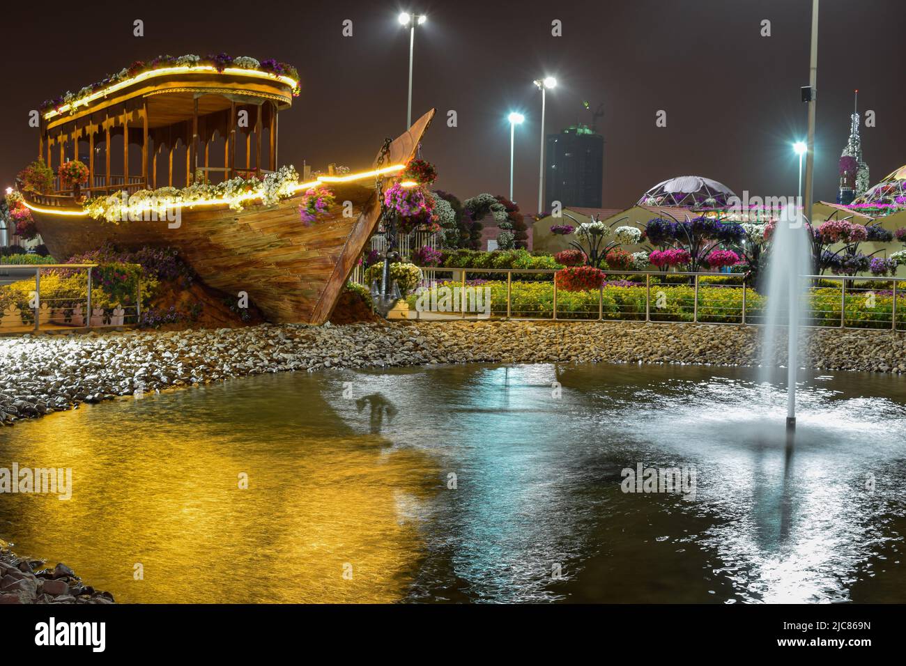 Nachtansicht eines Holzboots in der Nähe des Sees und des Brunnens im Dubai Miracle Garden. Stockfoto