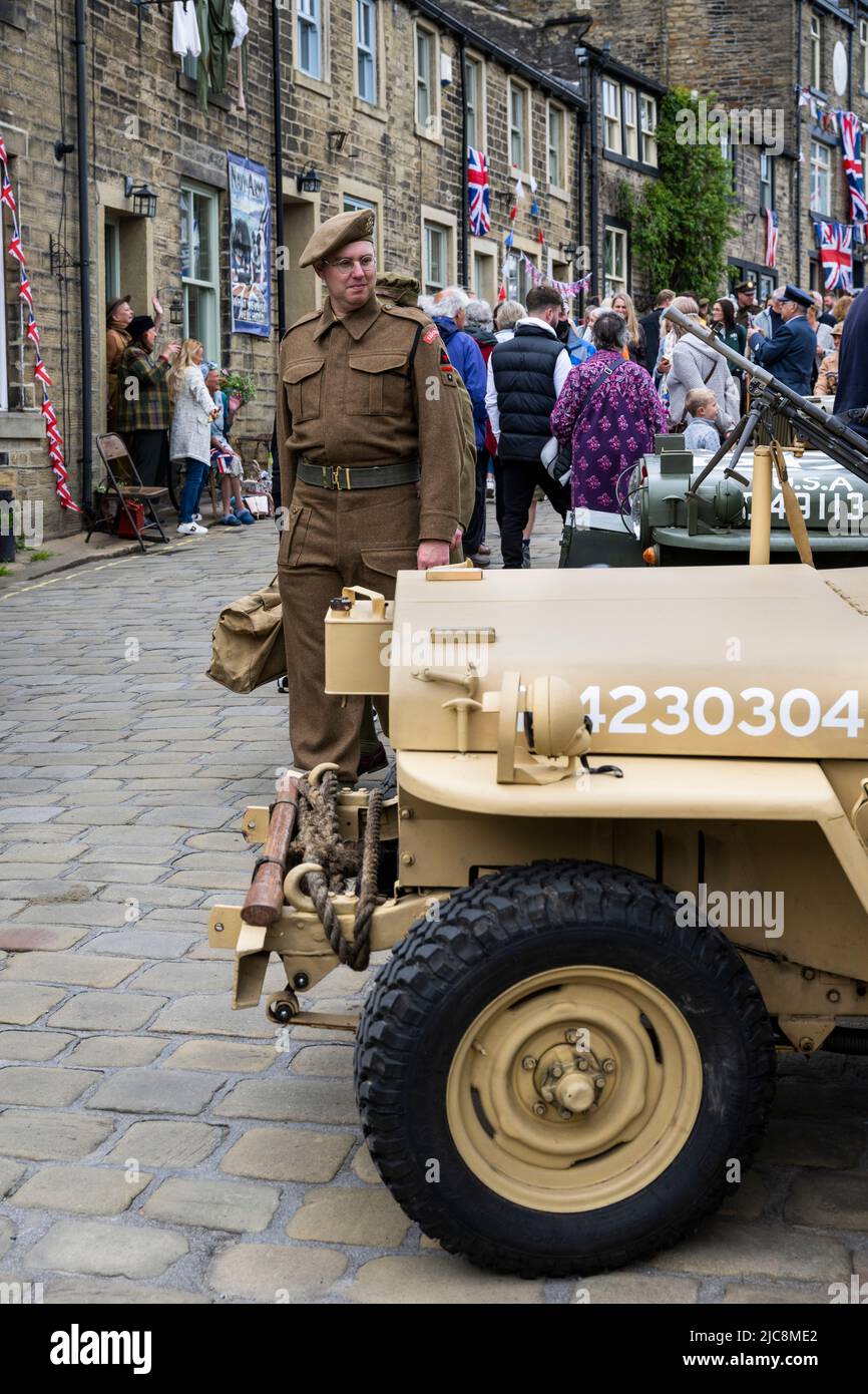 Haworth 1940er's Weekend (Mann in Khaki WW 2 Kostüm als Soldat mit Blick auf Jeep auf der geschäftigen steilen überfüllten Main Street) - West Yorkshire, England. Stockfoto