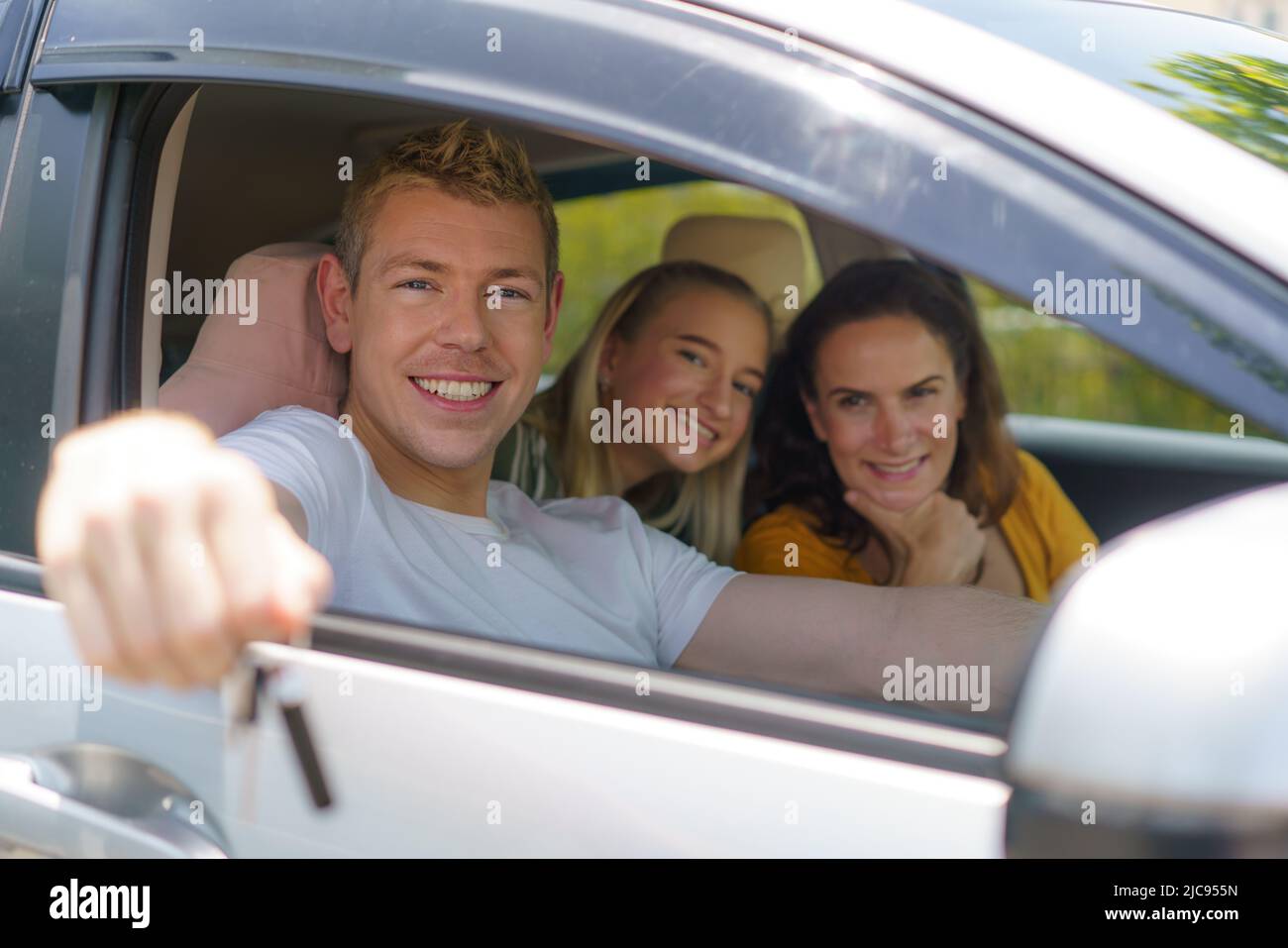 Kaukasischer Mann, der ein neues oder Mietauto kauft und den Schlüssel zeigt, sitzt im Auto. Stockfoto