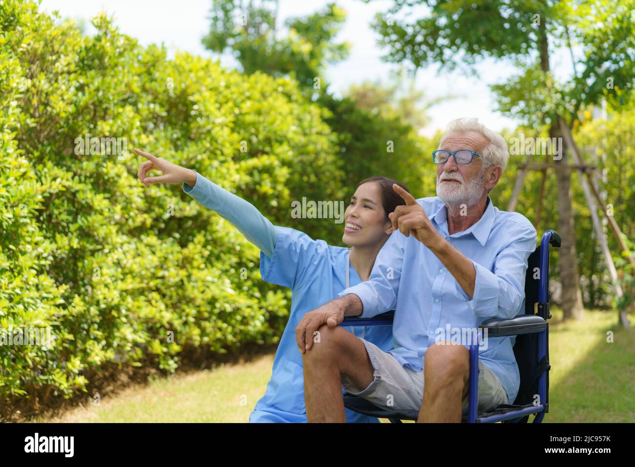 Asiatische Pflegekraft mit einem älteren Mann, der morgens im Garten auf dem Rollstuhl sitzt und die Natur nach Hause schaut. Stockfoto