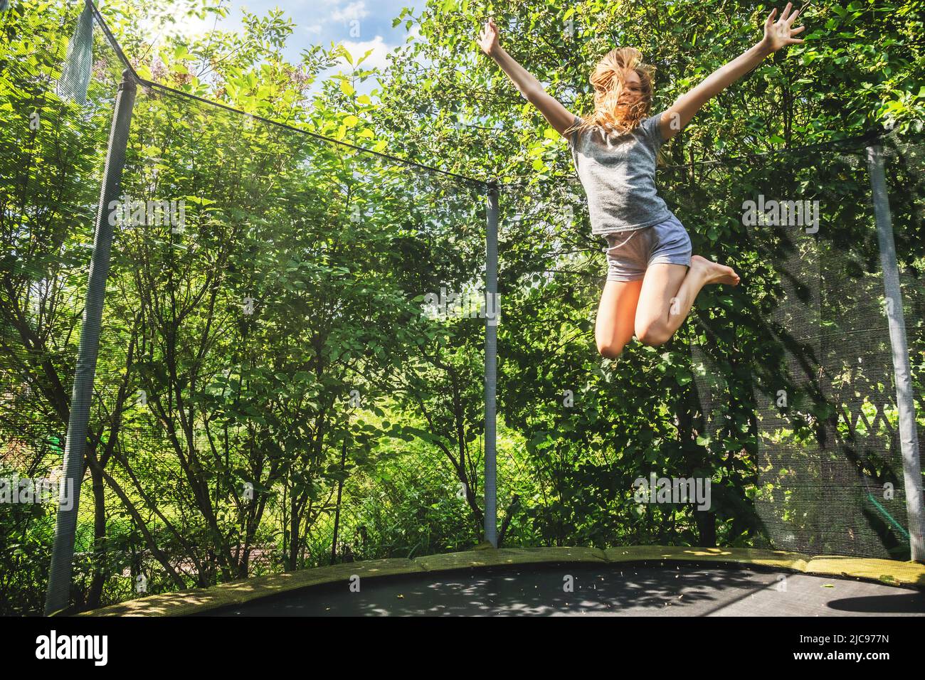 Präteen Mädchen mit Spaß hüpfen auf einem Trampolin in einem Hinterhof an einem Sommertag Stockfoto