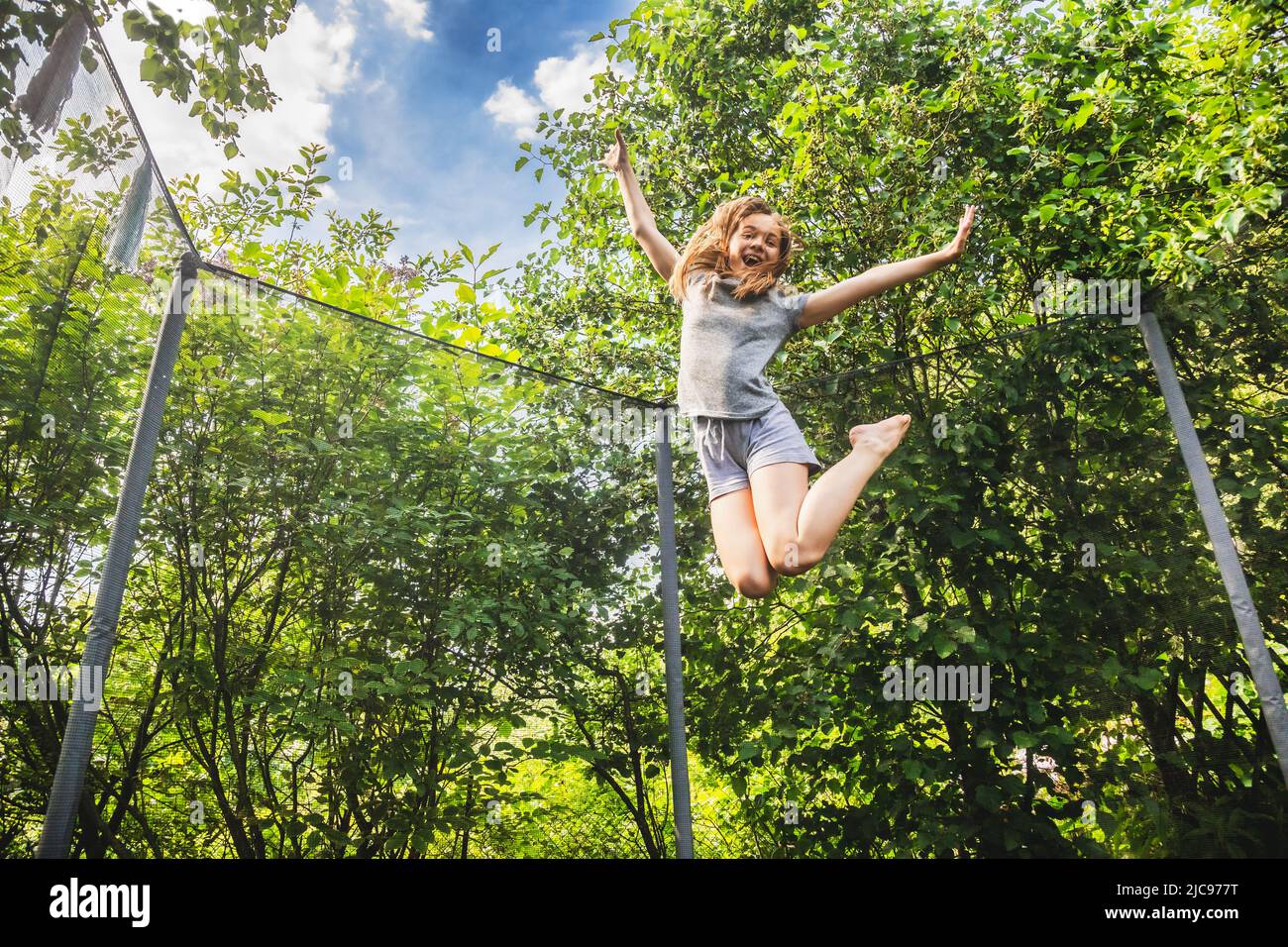 Präteen Mädchen mit Spaß hüpfen auf einem Trampolin in einem Hinterhof an einem Sommertag Stockfoto