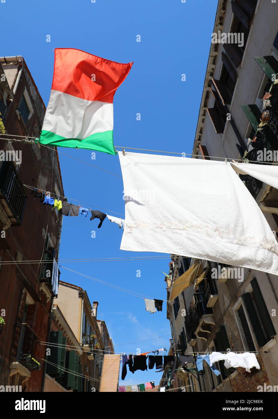 DIE ITALIENISCHE Flagge und die Kleidung hingen an sonnigen Tagen zwischen den Häusern der Stadt zum Trocknen auf Stockfoto