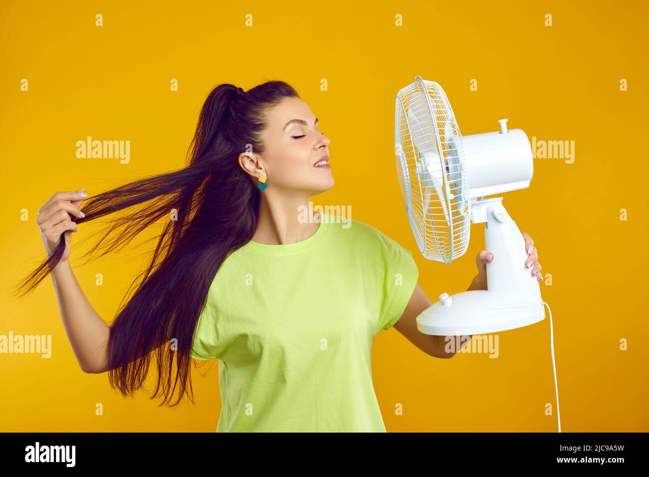 Frau genießt frische Luft und entweicht Sommerhitze mit elektrischem Ventilator isoliert auf orangefarbenem Hintergrund. Stockfoto