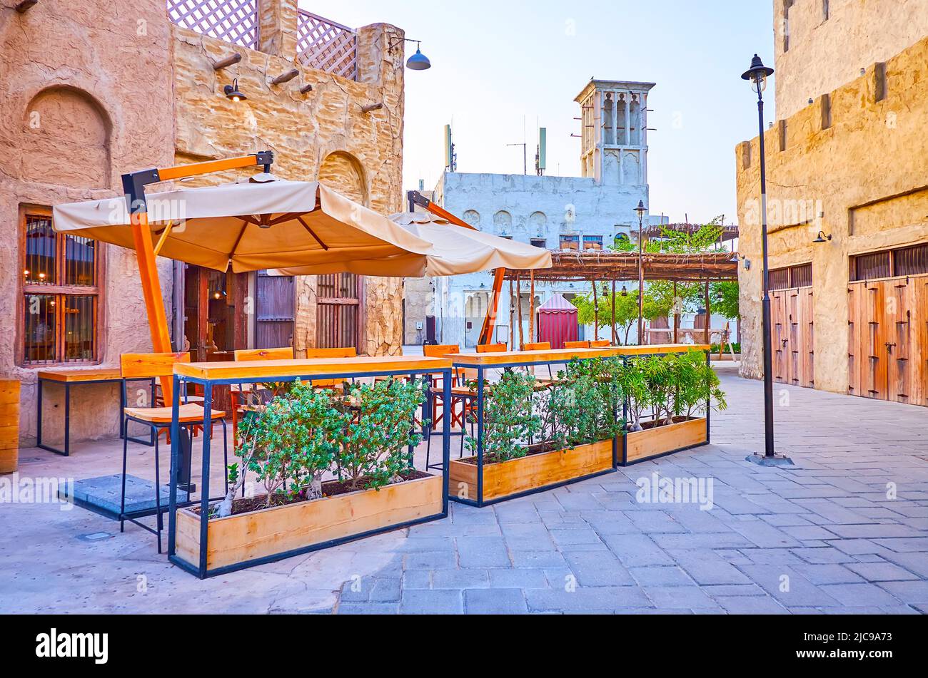 Die malerische Außenterrasse mit Holztischen, Stühlen und Sonnenschirmen vor dem Café befindet sich im adobe-Haus des alten Al Seef, Dubai, VAE Stockfoto