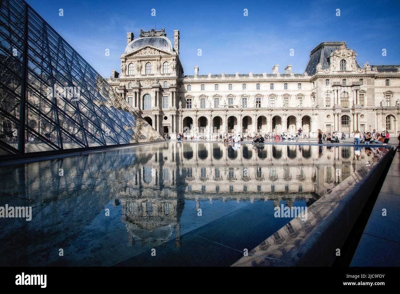 Touristen versammeln sich in der Nähe eines reflektierenden Pools im Innenhof des Louvre in Paris, Frankreich. Stockfoto