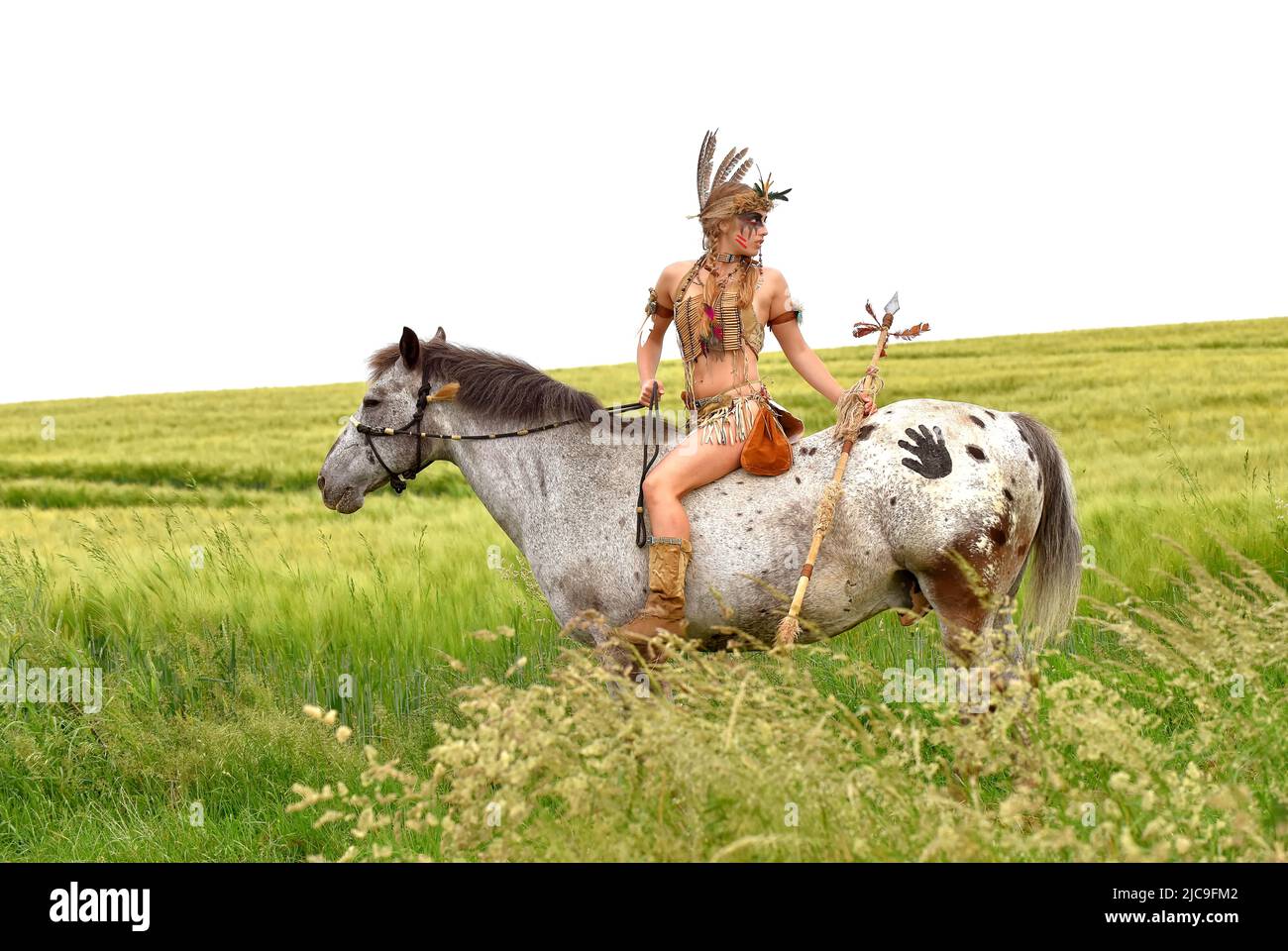 Ein junges indisches Mädchen wird im Prarie auf ihrem Pony reiten gesehen. Sie ist als Indianerin der Ureinwohner Amerikas verkleidet und hält einen Speer in der Hand. Stockfoto