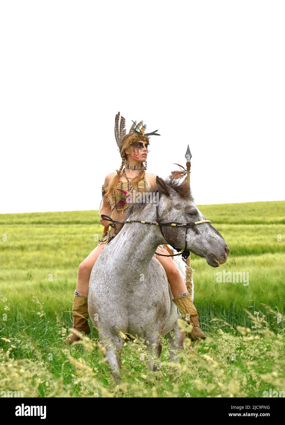 Ein junges indisches Mädchen wird im Prarie auf ihrem Pony reiten gesehen. Sie ist als Indianerin der Ureinwohner Amerikas verkleidet und hält einen Speer in der Hand. Stockfoto